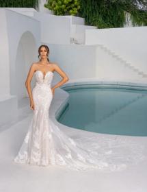 Model next to an elegant pool surrounded by white walls. The water is blue. The Kitty Chen H2437 wedding dress is white.