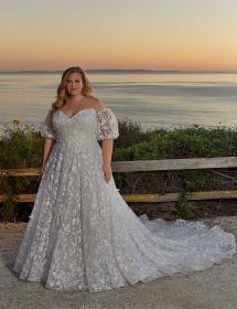Plus size model wearing a beautiful wedding dress in front of a beach scene